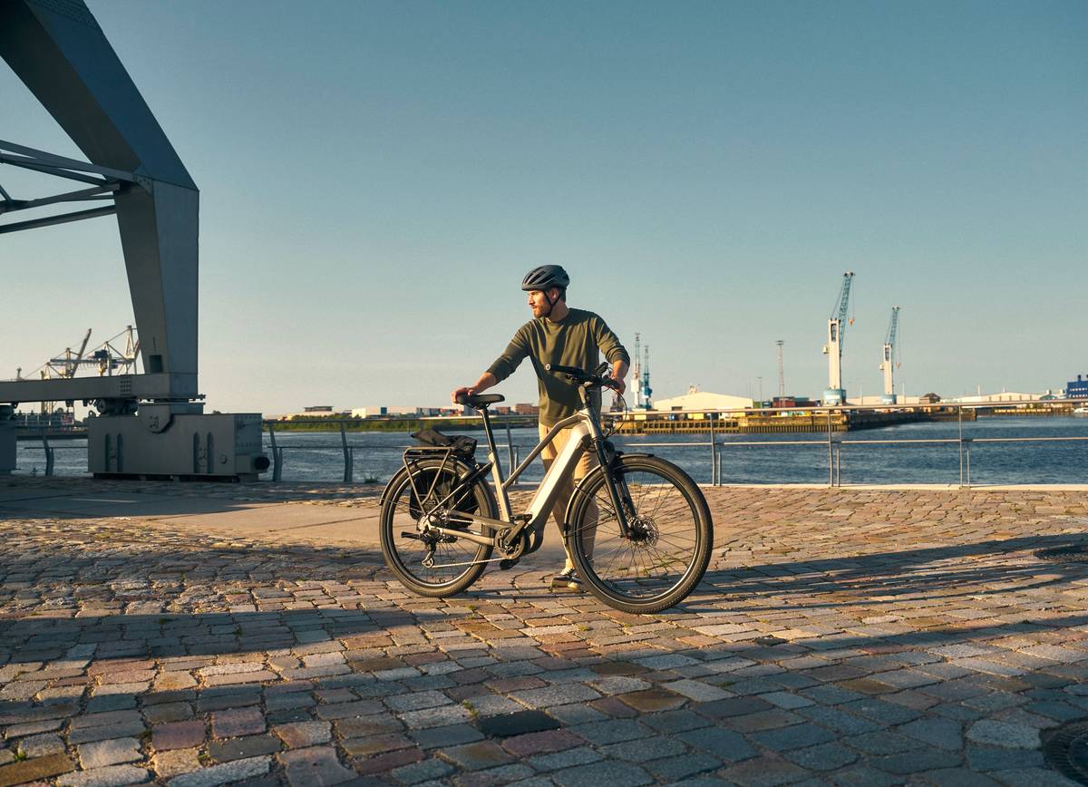 Mann mit E-Bike steht vor Hafenkulisse von Hamburg