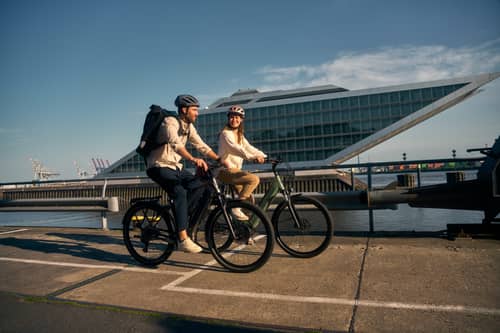 Paar fährt auf E-Bikes vor modernem Gebäude