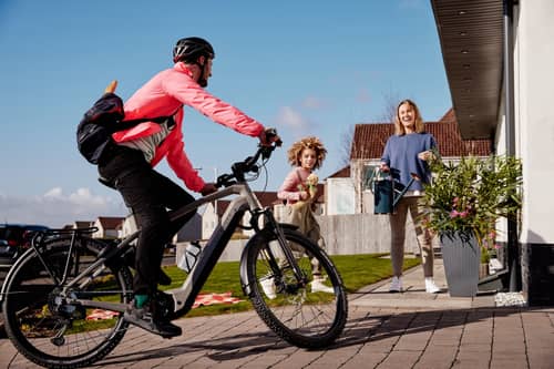 Familienvater kommt mit E-Bike nach Hause zu Frau und Kind