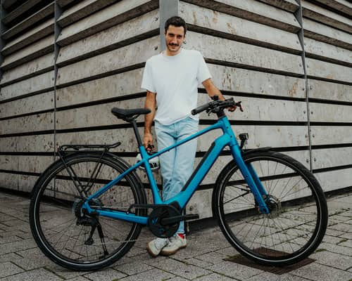 Man standing on the corner of a house with his blue e-bike