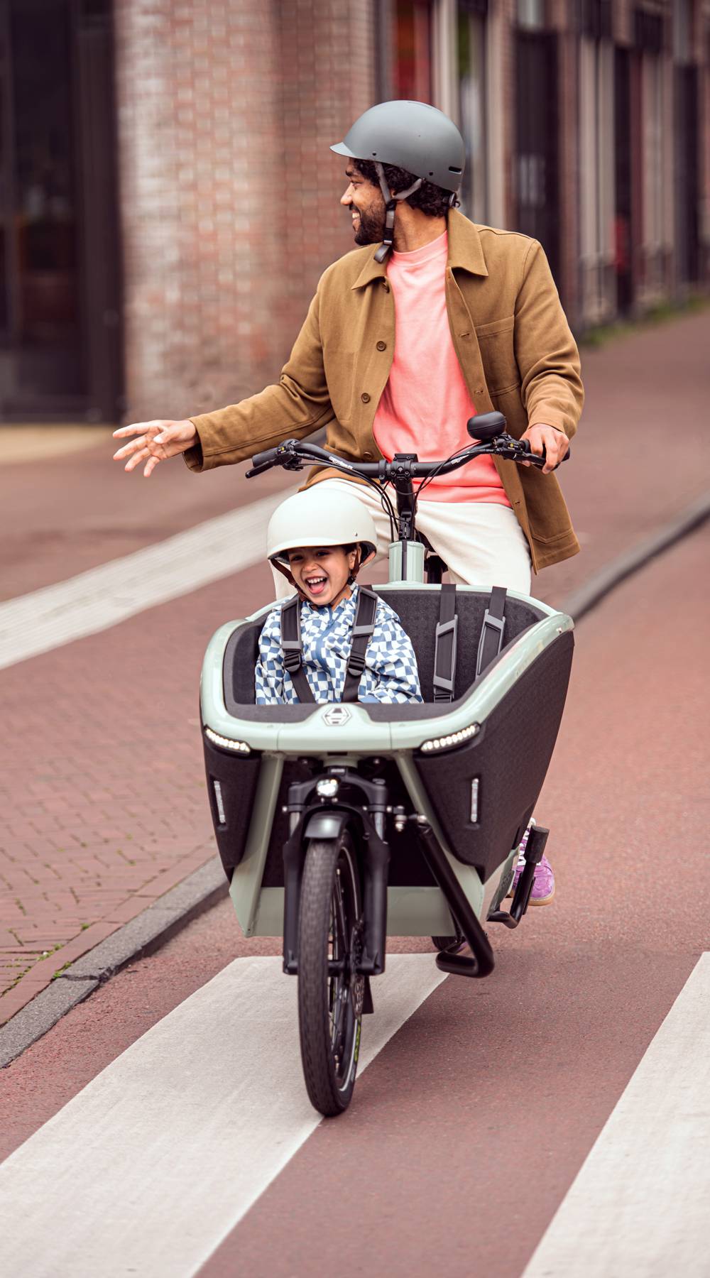 Vater fährt mit Kind im Lastenrad durch die Stadt