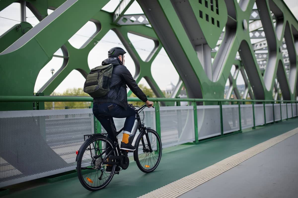 Man with a rucksack rides his bike over a bridge