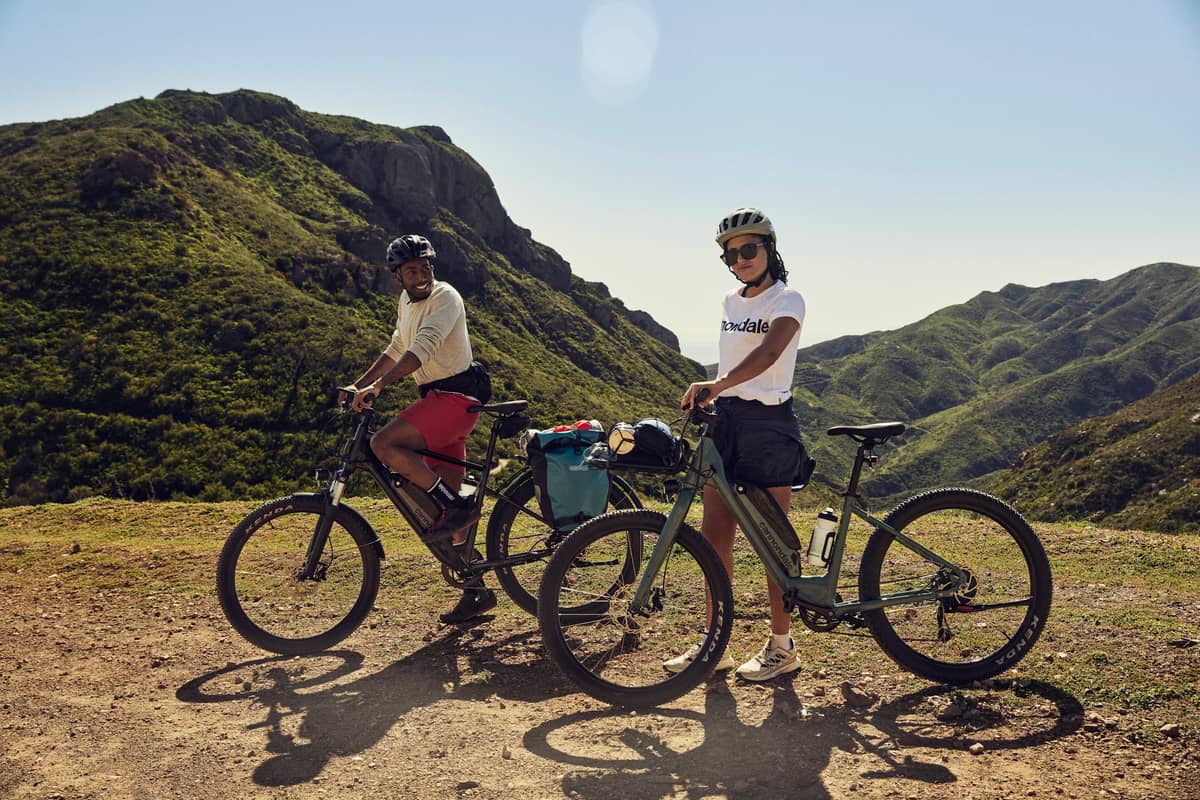 man and woman standing with bikes in front of mountain