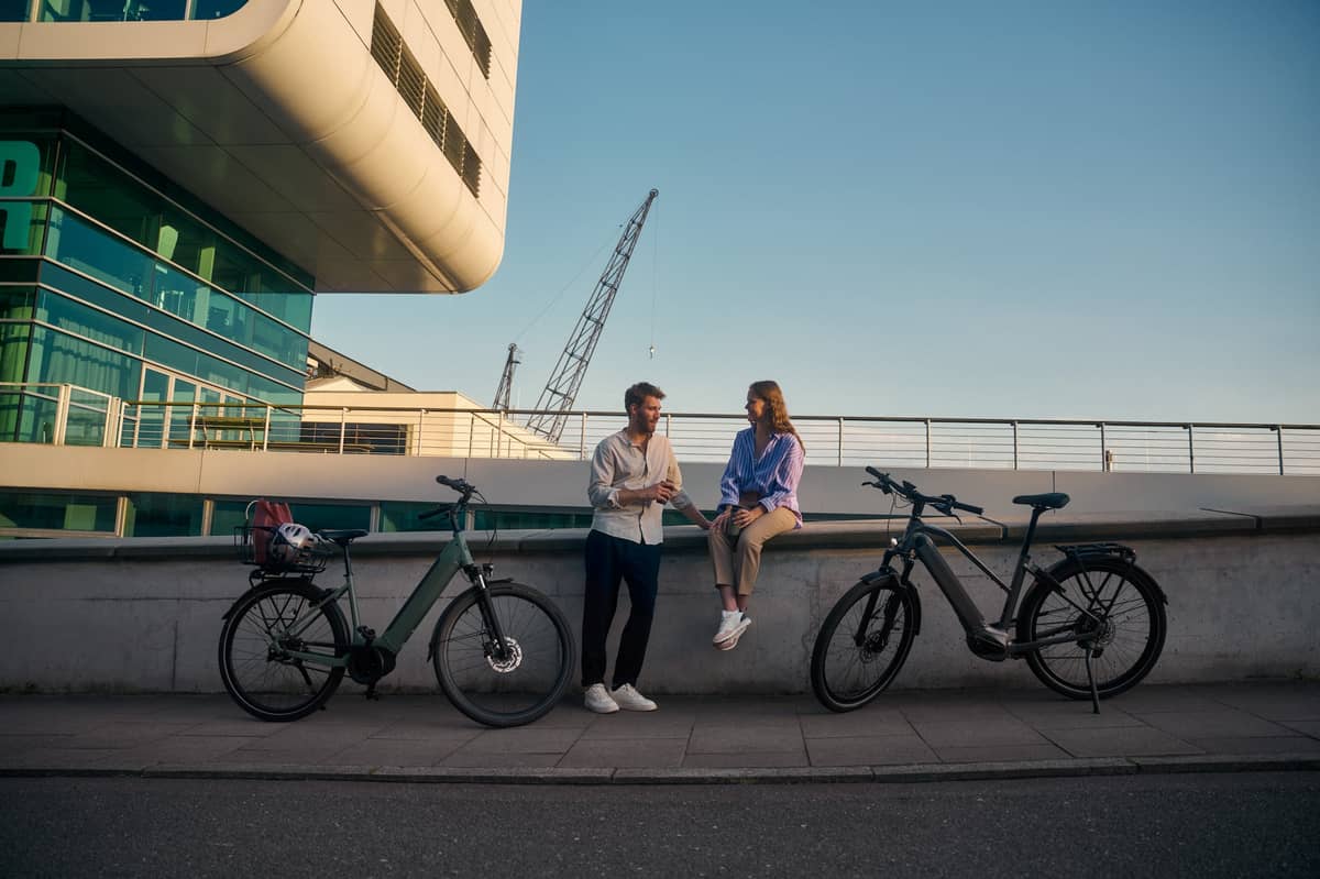 Two people sit on a wall and two bikes stand next to it