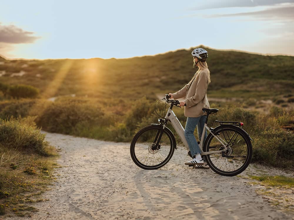 Frau mit Fahrrad in Dünen vor Sonnenuntergang