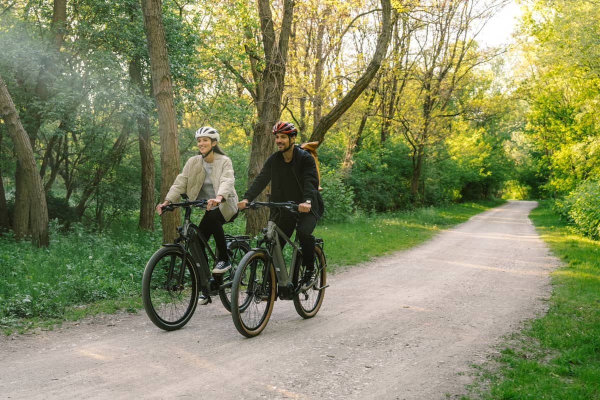 two people riding bikes on bike path in green surrounding